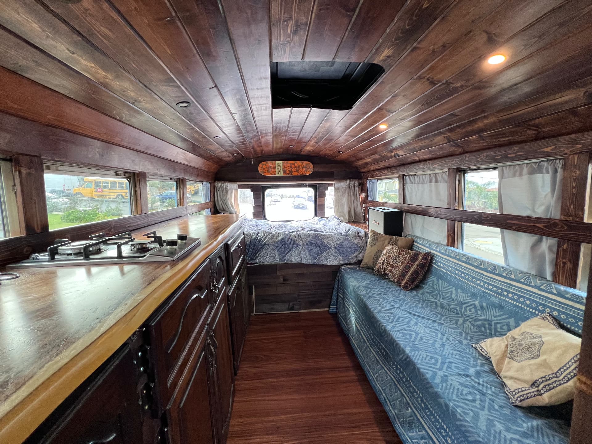 Skoolie conversion interior with dark wood plank ceiling, full kitchen and sleeping area