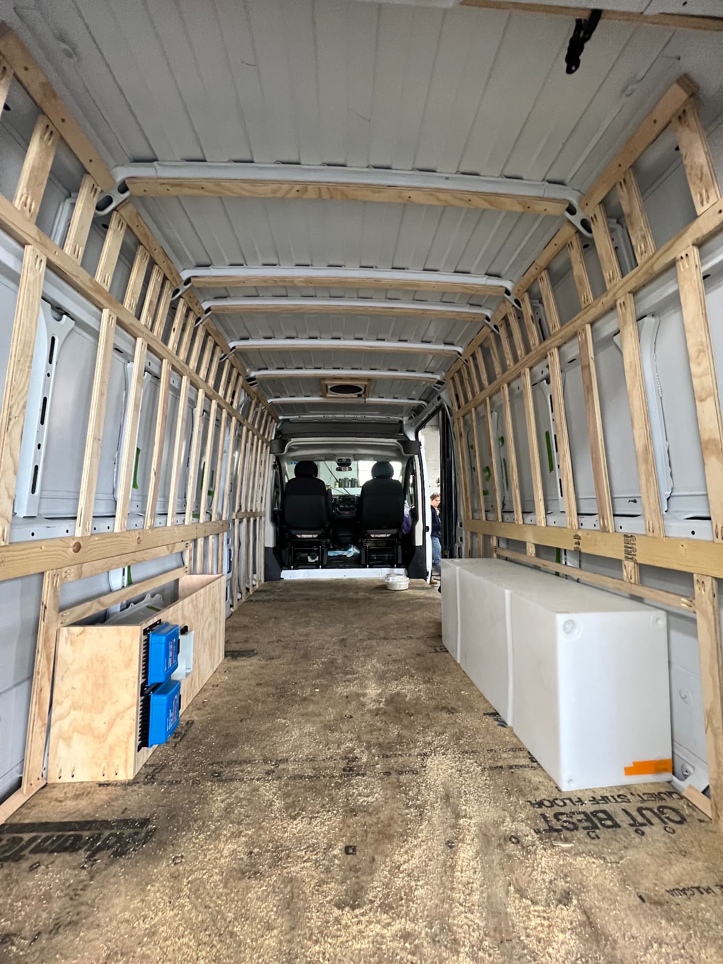 Camper van interior framed with wood strapping, fresh-water tanks and battery box during a build