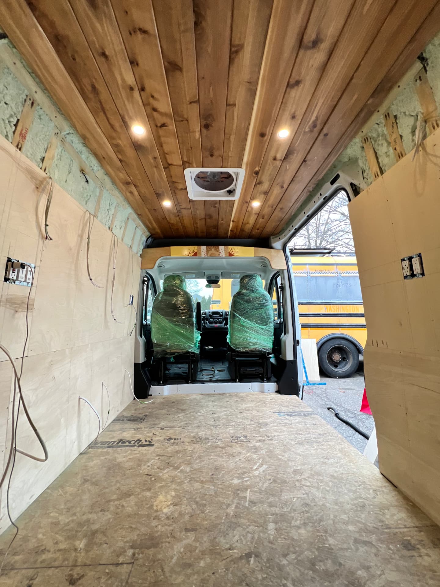 Camper van with cedar plank ceiling installed and wiring routed to wall outlets during a build