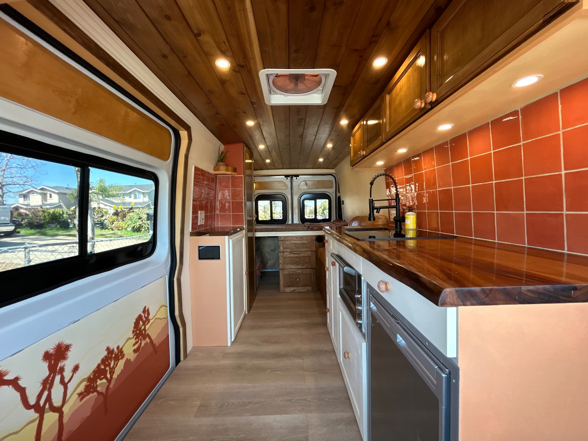 Camper van conversion galley kitchen with terracotta tile backsplash and wood ceiling