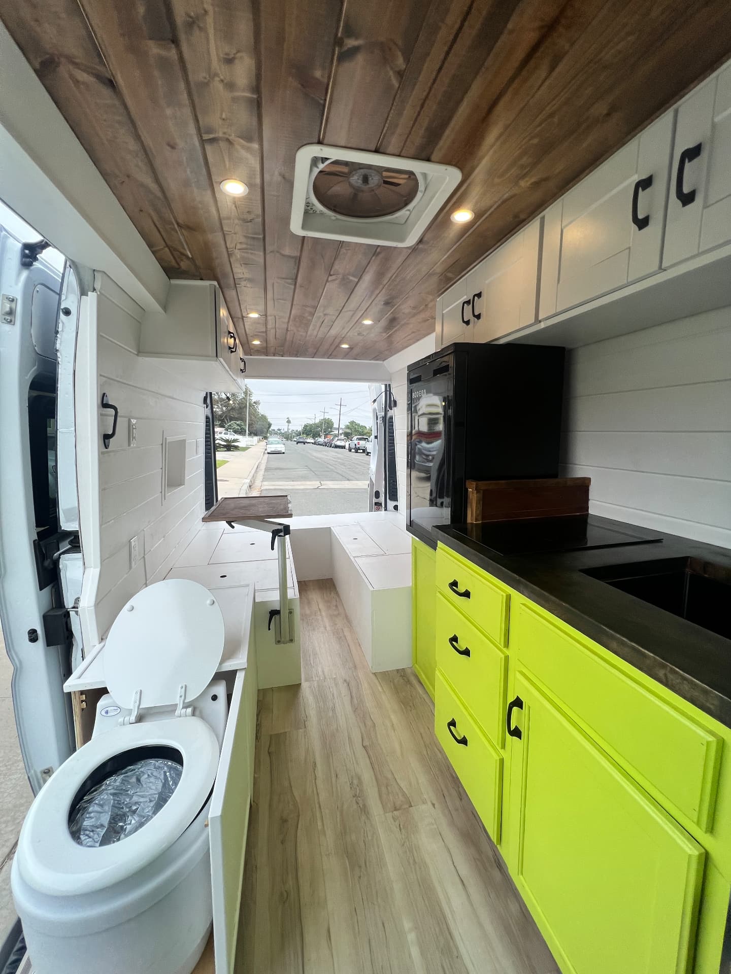 Camper van conversion interior with white shiplap walls, custom cabinets and composting toilet