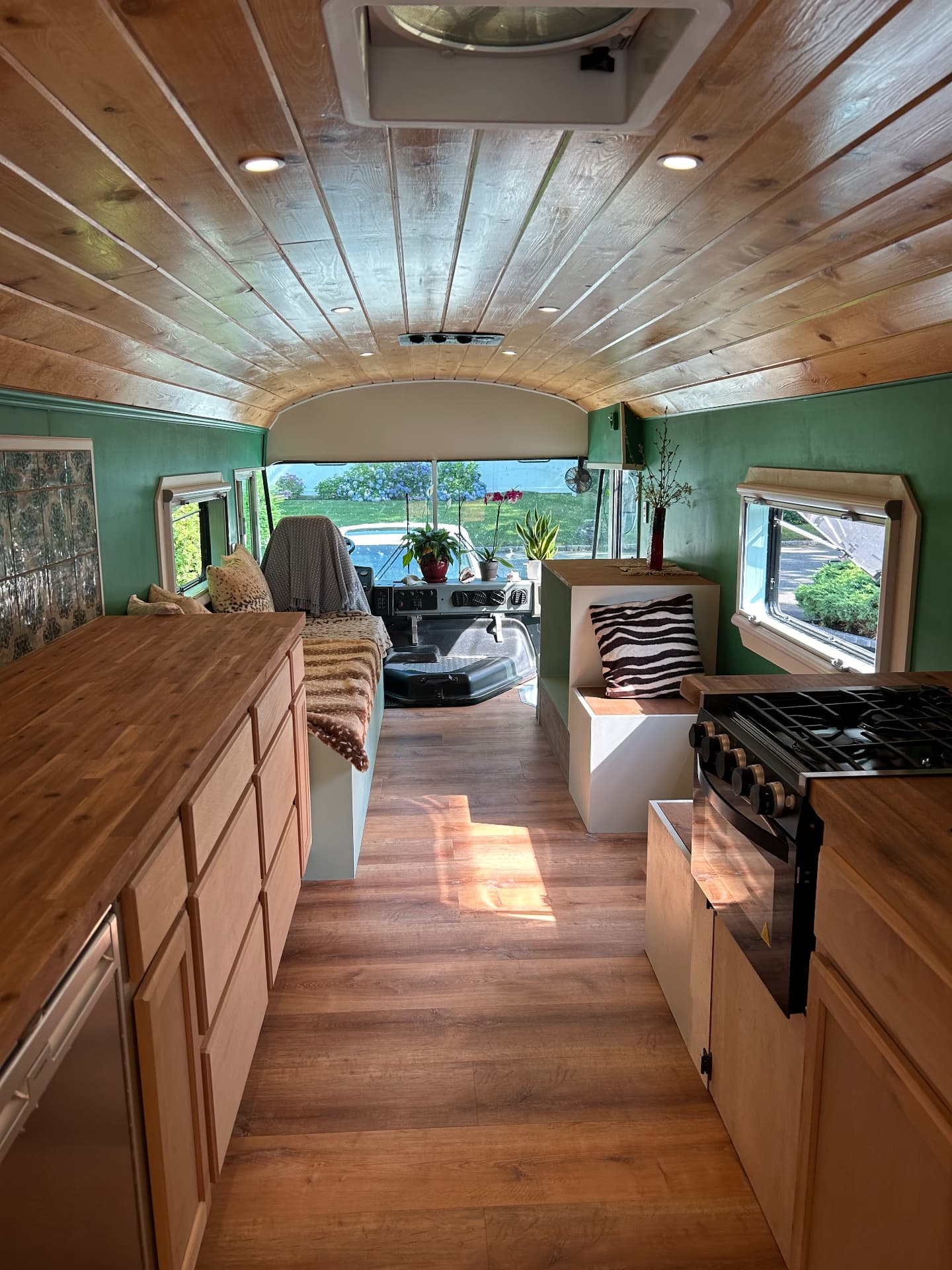 Finished skoolie interior with wood ceiling, kitchen and daylight through the windows
