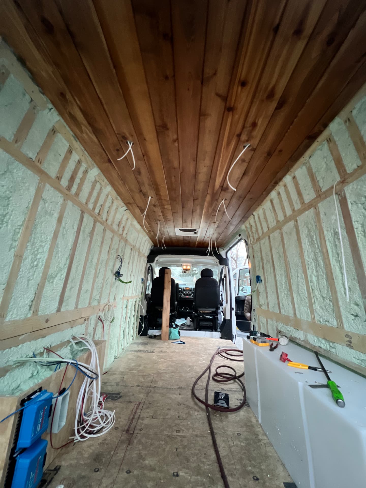 Camper van conversion with cedar plank ceiling and electrical wiring runs during a build