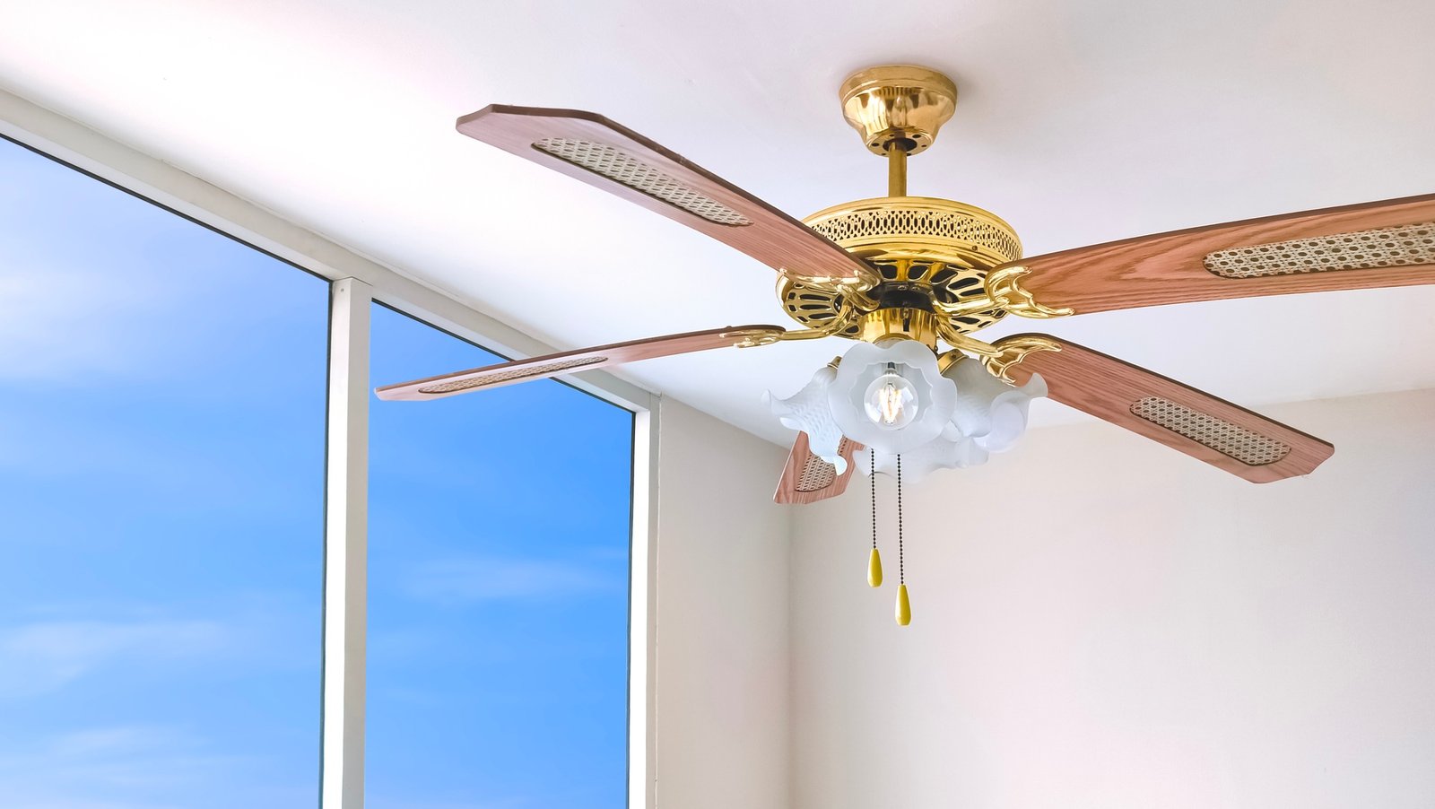 Vintage ceiling fan with electric lamps hanging on ceiling inside of white room